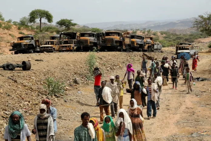 Villagers return from a market to Yechila town in south-central Tigray walking past burned vehicles, in Tigray, Ethiopia, on July 10, 2021 [File: Giulia Paravicini/Reuters]